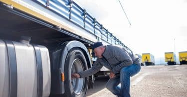 Un chauffeur poids lourd en train d'inspecter les pneus de son camion
