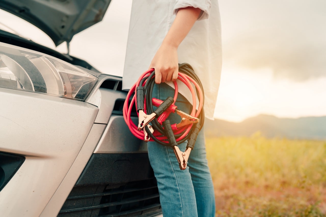 Une femme qui s'apprête à recharger la batterie de sa voiture à l'aide de câbles de recharge