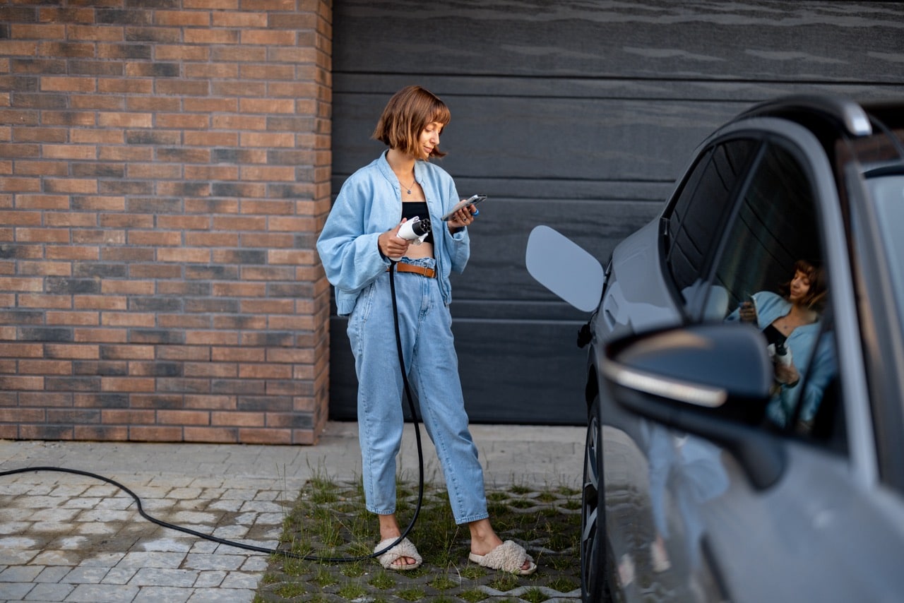 Une femme qui branche sa voiture électrique à la borne de recharge de sa maison