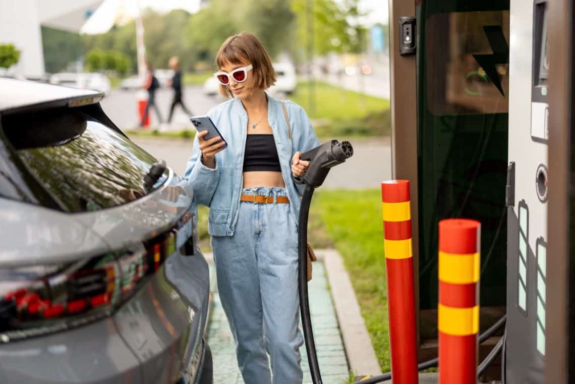 Une femme en train de recharger sa voiture électrique à une borne de recharge d'un supermarché