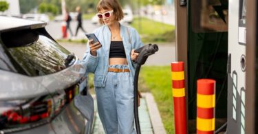 Une femme en train de recharger sa voiture électrique à une borne de recharge d'un supermarché