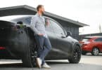Un homme souriant à côté de sa voiture électrique pour laquelle il paie une assurance auto peu chère