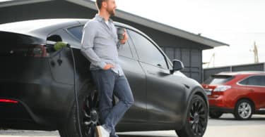 Un homme souriant à côté de sa voiture électrique pour laquelle il paie une assurance auto peu chère