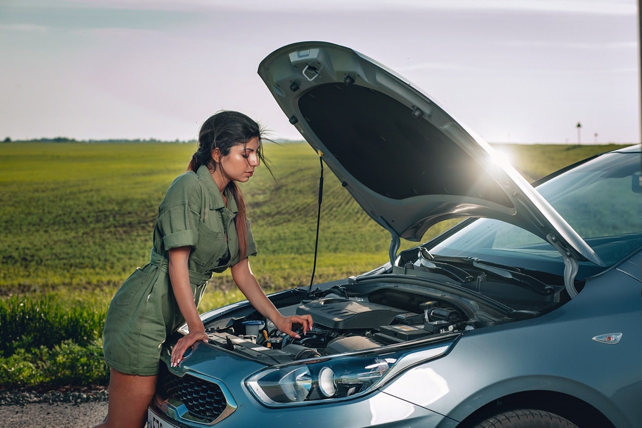 Une femme en train de vérifier les liquides de sa voiture. Elle est penchée au-dessus du moteur.