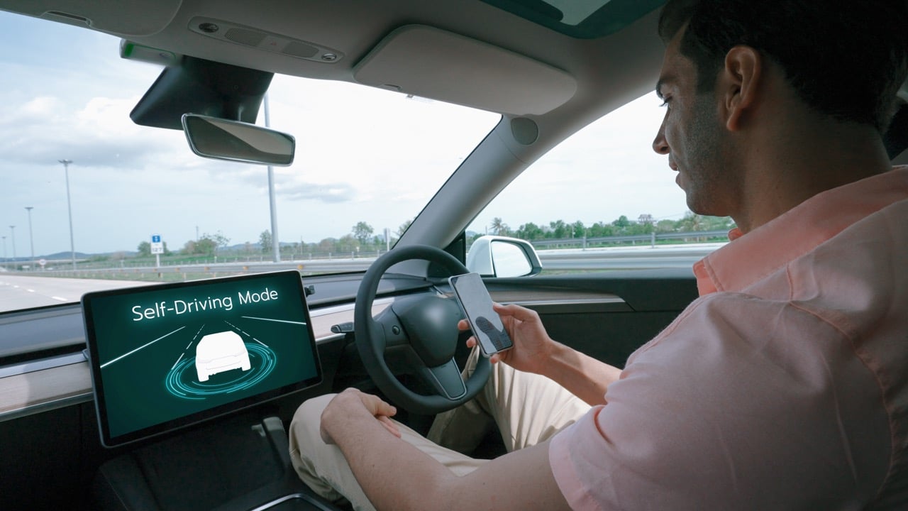 Un automobiliste en mode Autopilot dans sa Tesla. Il profite de son smartphone au volant